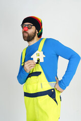 A clown in a bright costume holds a wooden house in his hands.