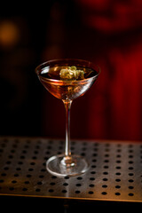 martini glass with alcoholic drink decorated with green plant of hop stands on bar