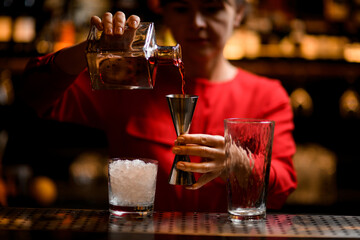 jigger in hand of female bartender in which she pours drink from bottle