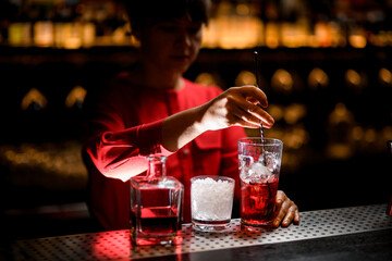 view on hand of woman bartender stirring by spoon drink with ice cubes in glass