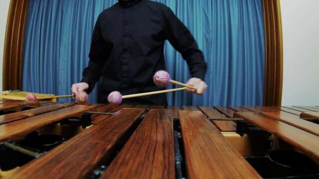 A male percussionist is playing tremolo on marimba wearing a black shirt. Sliding left ultra wide shot