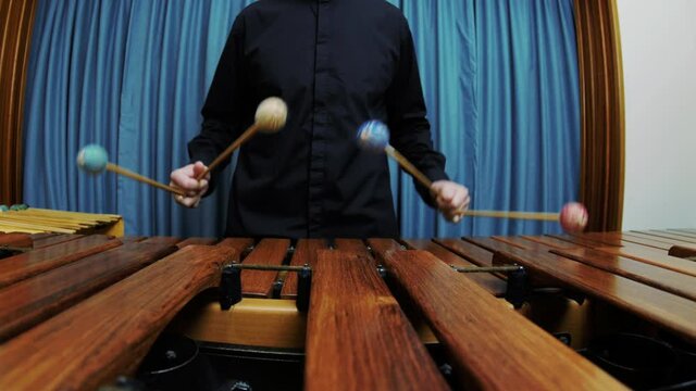A male percussionist is playing the marimba wearing a black shirt. Sliding right shot