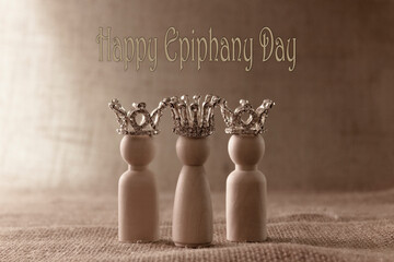 Three wise men figures with crowns on biege background and the text Happy Epiphany day. Copy space.