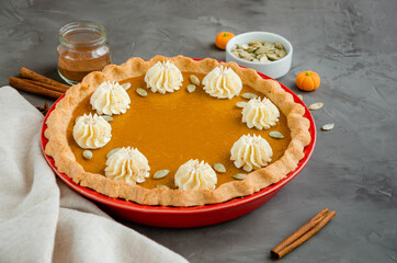 Traditional festive pumpkin pie with spices, whipped cream and seeds on top on a dark stone background. Dessert for Thanksgiving.