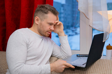 young man sits and works with laptop at home. concept of remote work in new year holidays