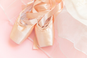 New pastel beige ballet shoes with satin ribbon and tutut skirt isolated on pink background. Ballerina classical pointe shoes for dance training. Ballet school concept. Top view flat lay, copy space