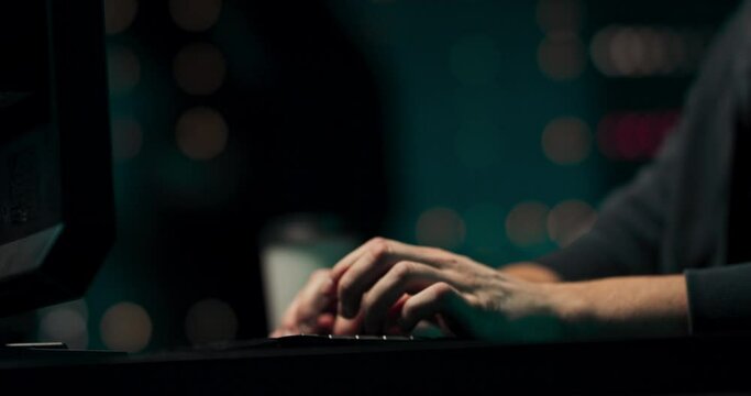 Close up of a young hackers hands writing malware on a computer keyboard in a secret hideout.
