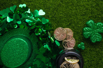 Shiny hat of leprechaun with clover and coins on green grass background. St. Patrick's Day...