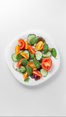 White plate with a bright fresh vegetable salad of vegetables and greens on a light background
