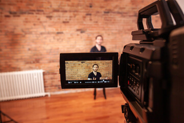 A closeup of a video camera, with shoot in progress as a man looks at the camera, in studio setting...