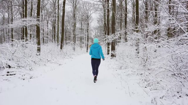 Young woman running down a path in the winter woods through snow