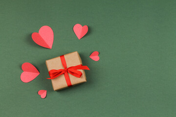 Gift box with bow and paper hearts on a green background. Valentine's Day.