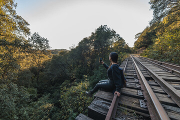 Girl scout walking and resting along the train tracks and a bridge in the middle of the forest, dressed in black with a blue backpack, black hat and backpack 11