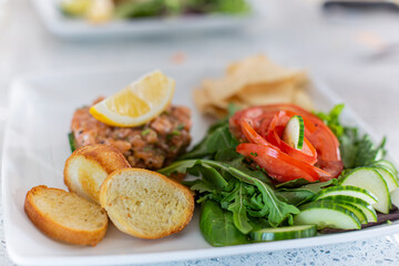 An aesthetic shot of French dish Tartare de saumon avec fleur de tomate, placed on a white plate, blurred background creates super focus on food. 