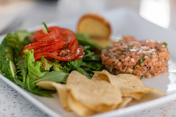 Close up shot of single serving of Tartare de saumon avec fleur de tomate, background has been blurred, along with edges of the food. 