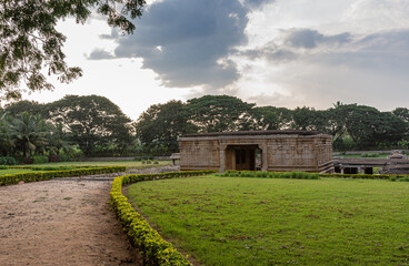 Hampi, Karnataka, India - November 4, 2013: Prasanna Virupaksha underground Shiva Temple. The dirt road to the entrance gate under sunset cloudscape with green foliage and grass around.