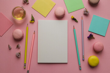 Creative feminine workspace with sketchbook for drawing, pencils, a cup of tea and macaroons on pink background. Art concept. Top view, flat lay