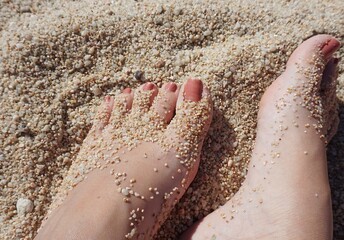 Pies descalzo de chica con pedicura sobre arena gruesa de la playa