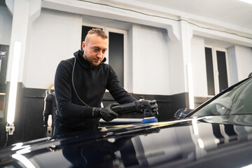 Detailing center worker polishes car body with polisher