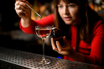 glass with liquid stands on bar and woman adds ingredient to it