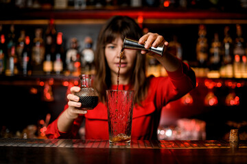 glass stands on bar and woman bartender masterfully pours drink from jigger into it