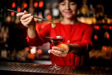 view of glass alcoholic with drink which female hand with tweezers carefully decorates with hop