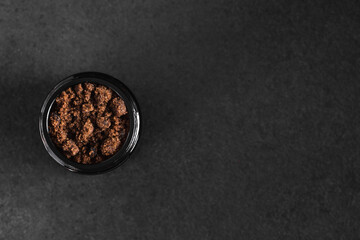 Dark muscovado sugar in a jar on black table with copy space. Top view.