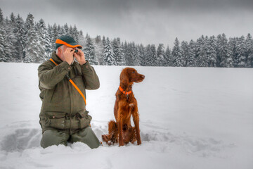 In winter a hunter kneels in the snow and observes his snowy hunting ground through a small...