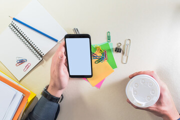 Top view of a male hands holding mobile phone, on a office desk.