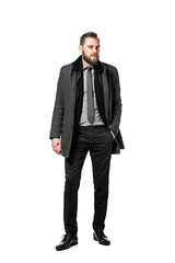 Fashionable and attractive bearded businessman standing against a white background, wearing a dark suit and tie with an overcoat looking in to camera.