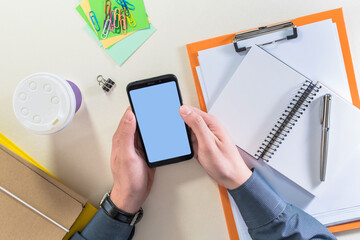 Top view of a male hands holding mobile phone, on a office desk.
