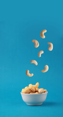 cashew pouring into white bowl against blue background. Concept of flying food