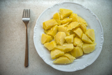 Boiled yellow potatoes on a white plate, next to a fork.