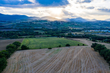 Aerial view of warm sunset on the hills surrounding Fabriano, Marche, Italy. It's summer and the sun is lighting the cultivated fields.