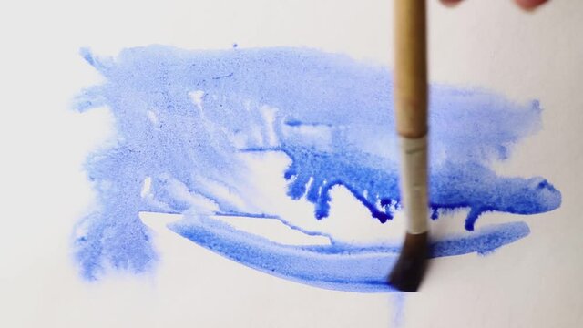 brush strokes of watercolor blue paint with stains on a sheet of white paper.