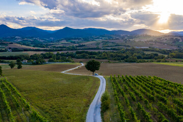 Aerial view of a winding road on the hills surrounding the town of Fabriano, in the Italian Marche region. A car is parked on a lonely road during a wonderful sunset. - obrazy, fototapety, plakaty