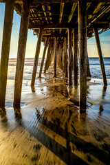 Pacific Ocean rising tide under pier with sand and reflection of water