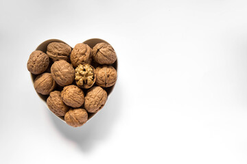 Whole walnuts and one cracked broken heart in a white heart-shaped bowl on a white background. Top view. Place for text.