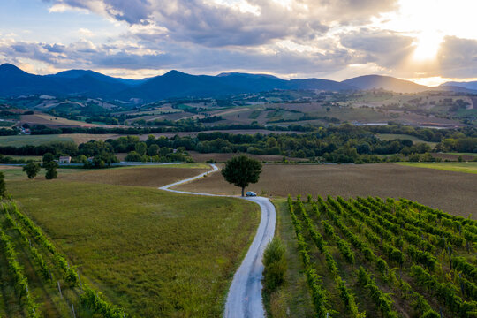 Aerial view of a winding road on the hills surrounding the town of Fabriano, in the Italian Marche region. A car is parked on a lonely road during a wonderful sunset.