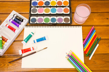 Wooden background with set of color pencils used water color box, tube colors