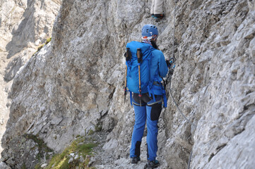 Fototapeta premium Kobieta ubrana na niebiesko idzie wąską, skalną półką na via ferracie w Dolomitach