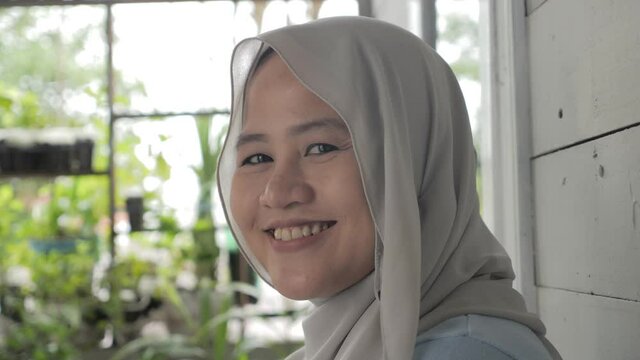 Portrait of beautiful Asian muslim woman smiling at camera, woman stiting relaxing outside her home