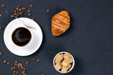 A cup of hot coffee and croissants on a black background. Breakfast with coffee and fresh pastry. Coffee beans on a table. Fresh cake and pastry. Flat lay. Copy space. Place for text.