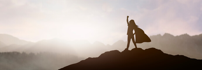 silhouette of a girl who dreams of being a superhero in a beautiful mountain landscape with a raised fist - obrazy, fototapety, plakaty