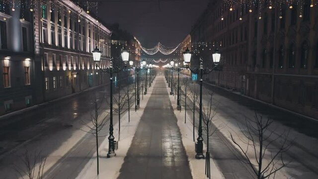 Night snowfall on a beautiful old city street. New Year's lights, garlands. Drone video.