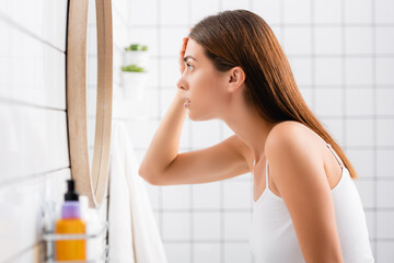 side view of worried young woman touching forehead while looking in mirror