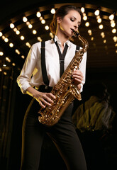 Gorgeous brunette model woman in fashionable formal suit with saxophone