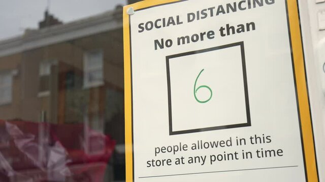 SOCIAL DISTANCING - no more than 6 people allowed in store at any point in time. Coronavirus COVID-19 pandemic text message board sticker warning at the entrance of a shop in 4K.