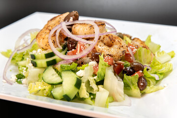 Shrimp Greek Salad stacked high on the plate with healthy vegetables and restaurant quality presentation