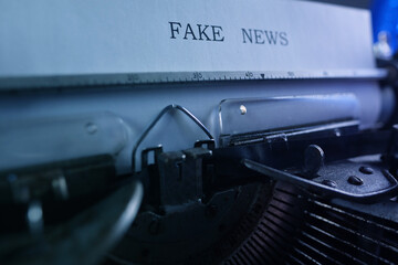 old typewriter on table, words fake news are printed on paper in large size, candle is burning,...